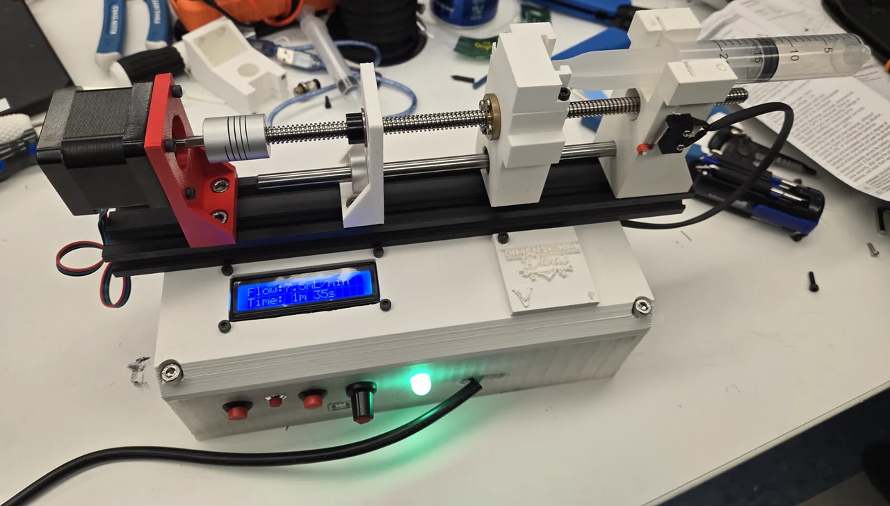 The assembled syringe pump on a bench, a syringe clamped in the carriage and the controller box sitting under the rail.